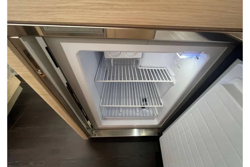 Fonn Taistil Domhain Yacht Photos Pics Open refrigerator inside a 2025 Fountaine Pajot 41 yacht, featuring empty wire shelves.