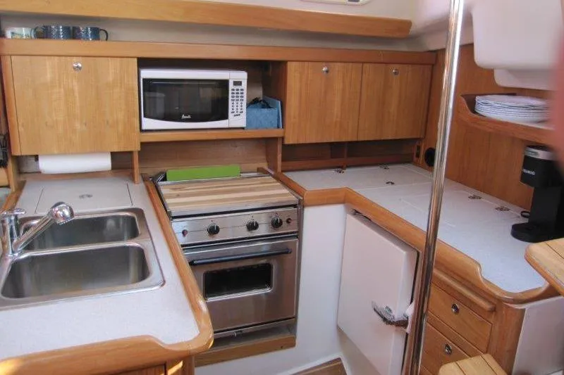 Sassy Cat Yacht Photos Pics Compact kitchen in a 2004 Catalina 350 MkII sailboat with wooden cabinets and modern appliances.