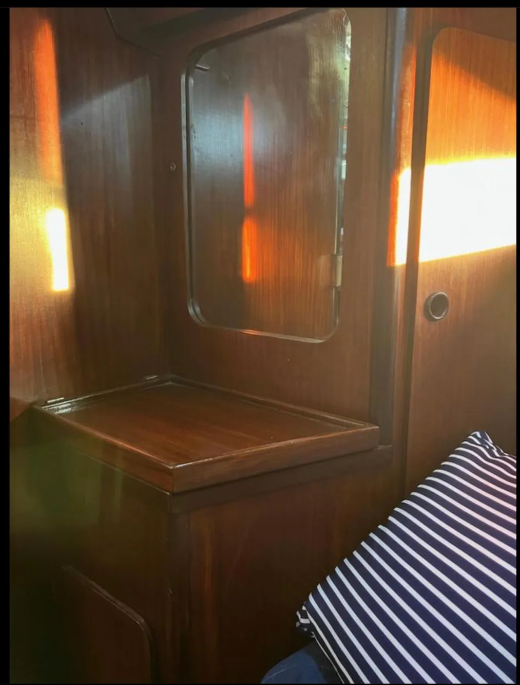 Interior of 1985 Gib'Sea 126 sailboat with wooden cabinetry and striped cushion.
