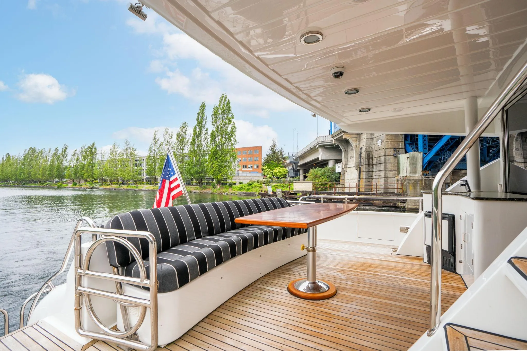 Outdoor seating area on 1999 Vitech 68' Pilothouse yacht with American flag and scenic river view.