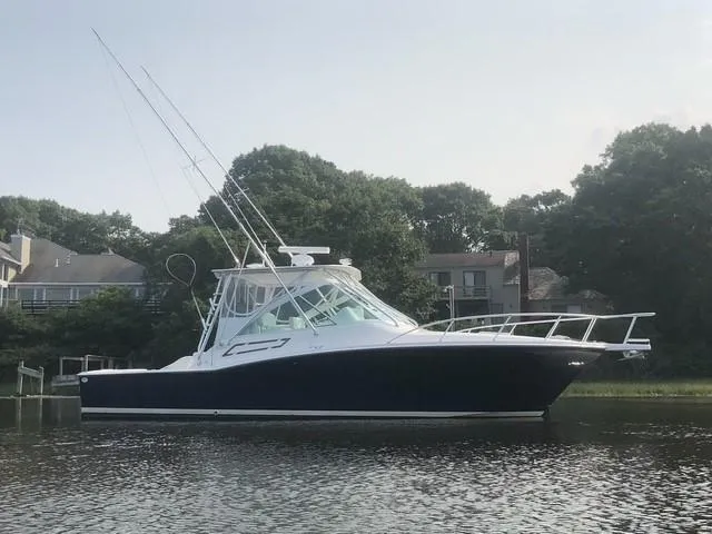 Arbutus Yacht Photos Pics 2006 Cabo 32 Express HT boat on calm water, surrounded by trees and houses.