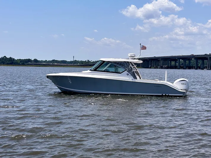  Yacht Photos Pics 2024 Pursuit DC 295 Dual Console boat cruising on a sunny day near a bridge.