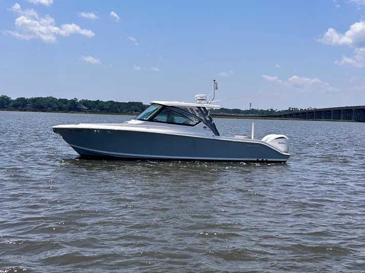  Yacht Photos Pics 2024 Pursuit DC 295 Dual Console boat on calm water under a clear blue sky.