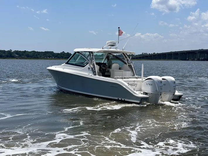  Yacht Photos Pics 2024 Pursuit DC 295 Dual Console boat cruising on a sunny day with bridge in background.