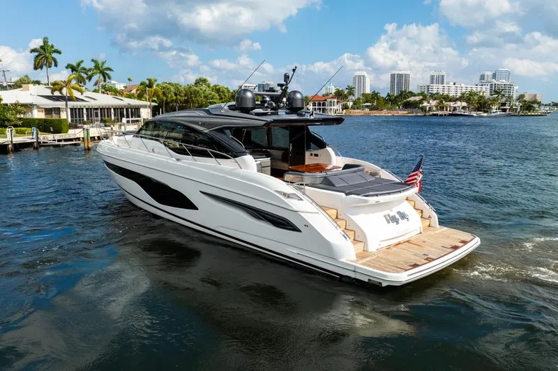 Fly By Yacht Photos Pics 2019 Princess V65 yacht cruising on a sunny day, with cityscape and palm trees in the background.
