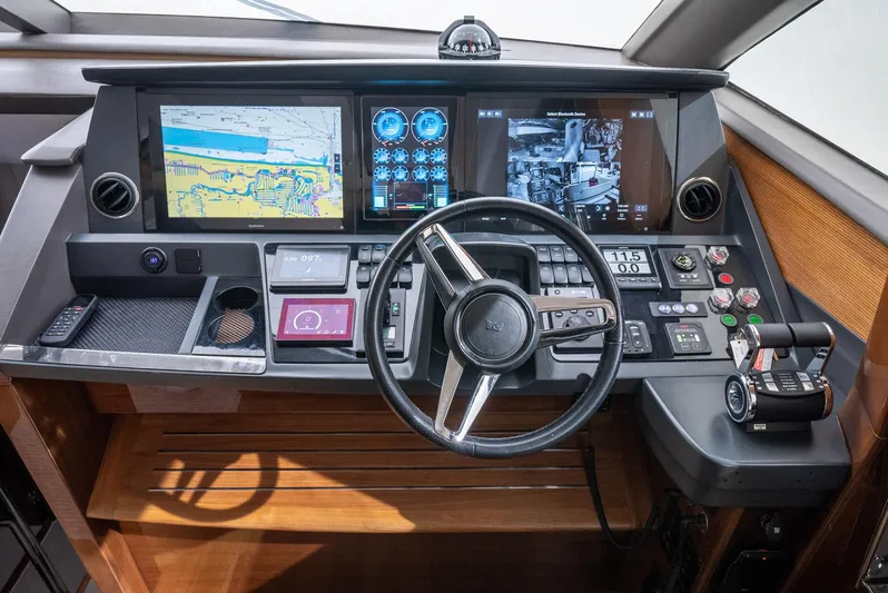 Fly By Yacht Photos Pics Control panel of a 2019 Princess V65 yacht with navigation screens and steering wheel.