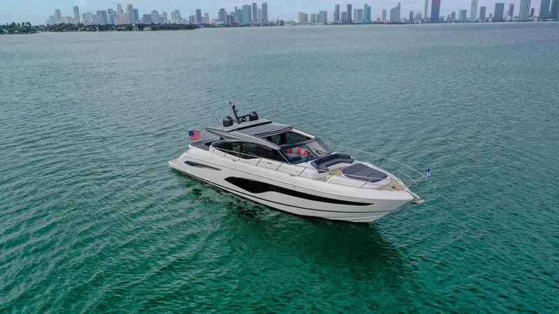 Fly By Yacht Photos Pics Luxury 2019 Princess V65 yacht cruising in open water with city skyline backdrop.