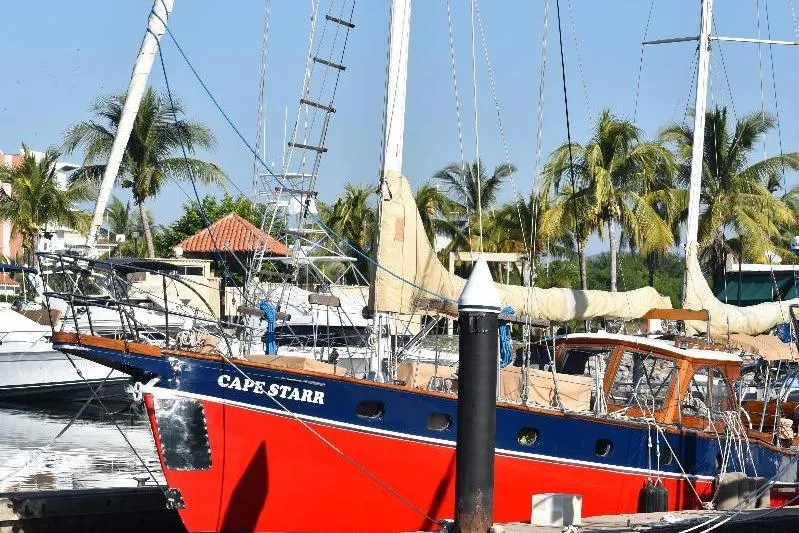 Red and blue 1958 Custom Steel Motorsailor docked, surrounded by palm trees.