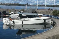 2022 Saxdor 320 GTC boat docked by a scenic waterfront under a partly cloudy sky.
