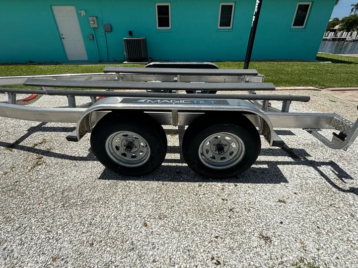  Yacht Photos Pics 2024 Lake & Bay 25 Open boat trailer parked on gravel near turquoise building.