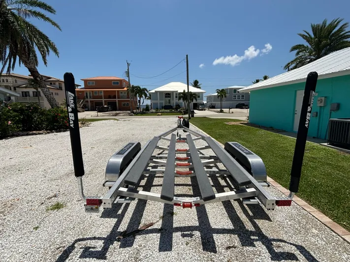  Yacht Photos Pics 2024 Lake & Bay 25 Open boat trailer on gravel driveway, sunny day.