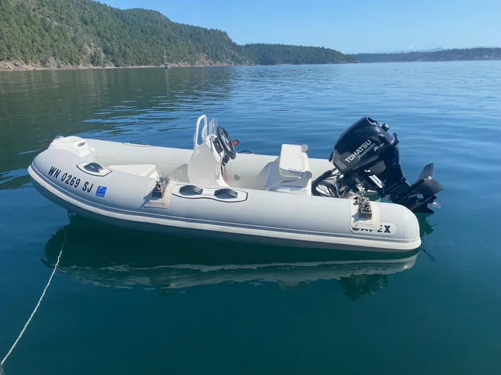 Carina Yacht Photos Pics Inflatable boat with Tohatsu motor on calm water, near forested shoreline.