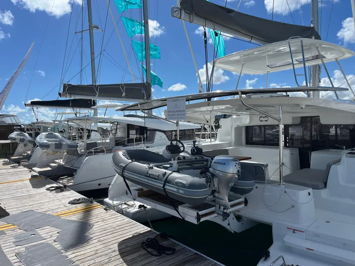  Yacht Photos Pics 2025 Lagoon 46 catamaran docked with inflatable boat, under clear blue sky.