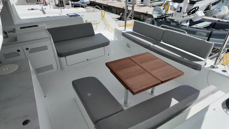  Yacht Photos Pics 2025 Lagoon 46 yacht cockpit with gray seating and wooden table, docked at marina.