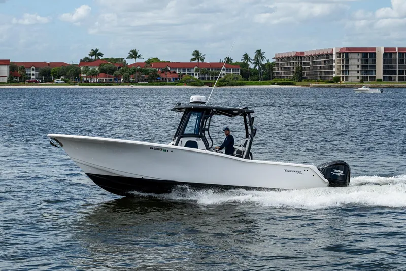 Floating Stones Yacht Photos Pics 2022 Tidewater 292 CC Adventure boat cruising on a scenic waterway near coastal buildings.