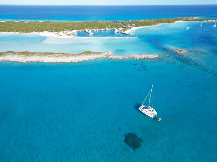 Buena Vida Yacht Photos Pics Aerial view of 2023 Lagoon 50 catamaran sailing in clear turquoise waters near a tropical island.