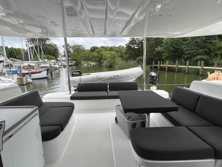 Buena Vida Yacht Photos Pics 2023 Lagoon 50 yacht interior with sleek seating and table, docked by lush greenery.