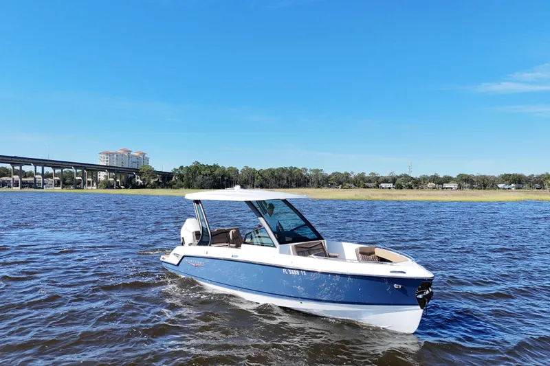  Yacht Photos Pics 2025 Monterey Elite 27 OB boat cruising on a sunny day, near a bridge and buildings.