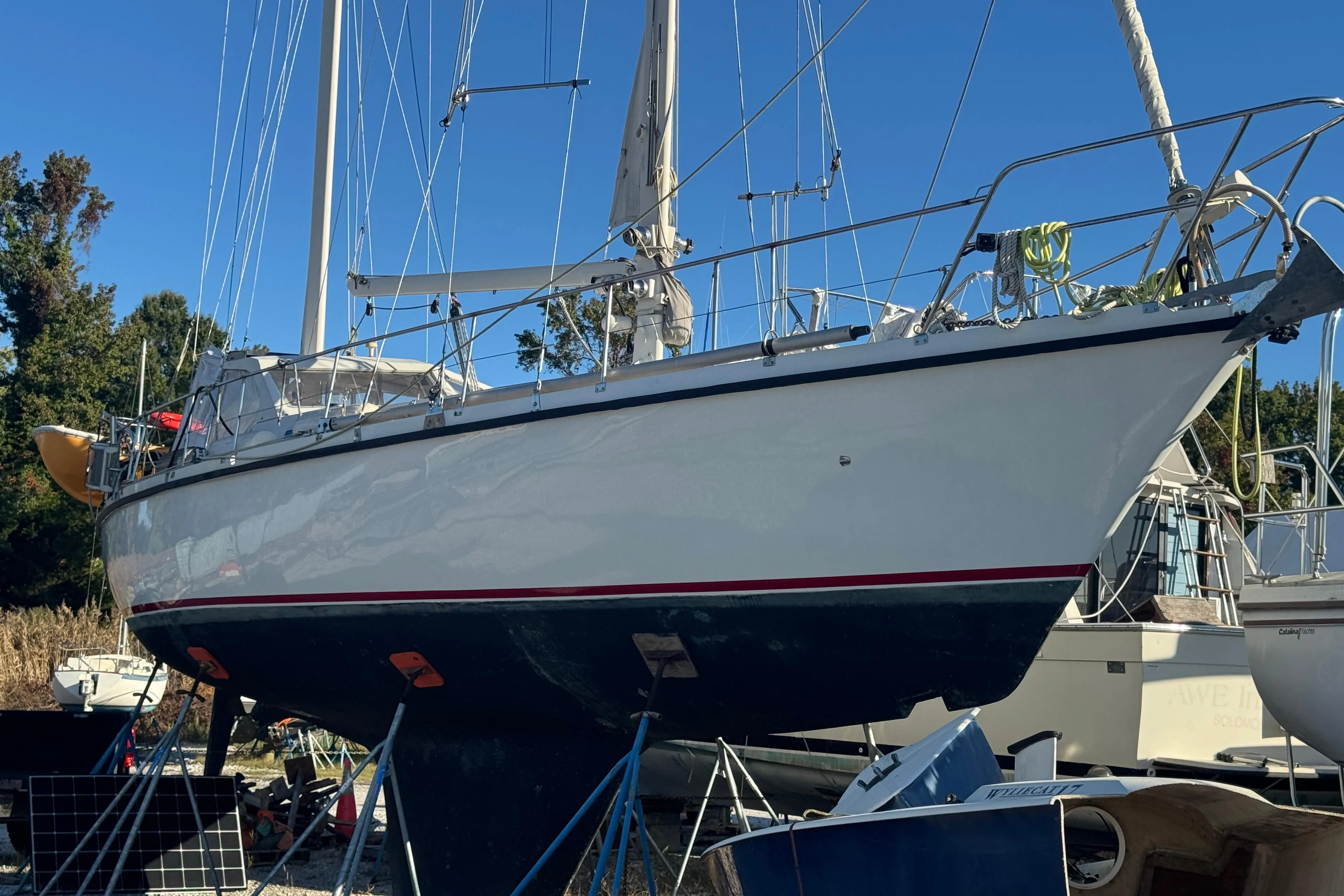 1988 Amel Sharki sailboat on dry dock, white hull, blue and red stripe, clear sky.