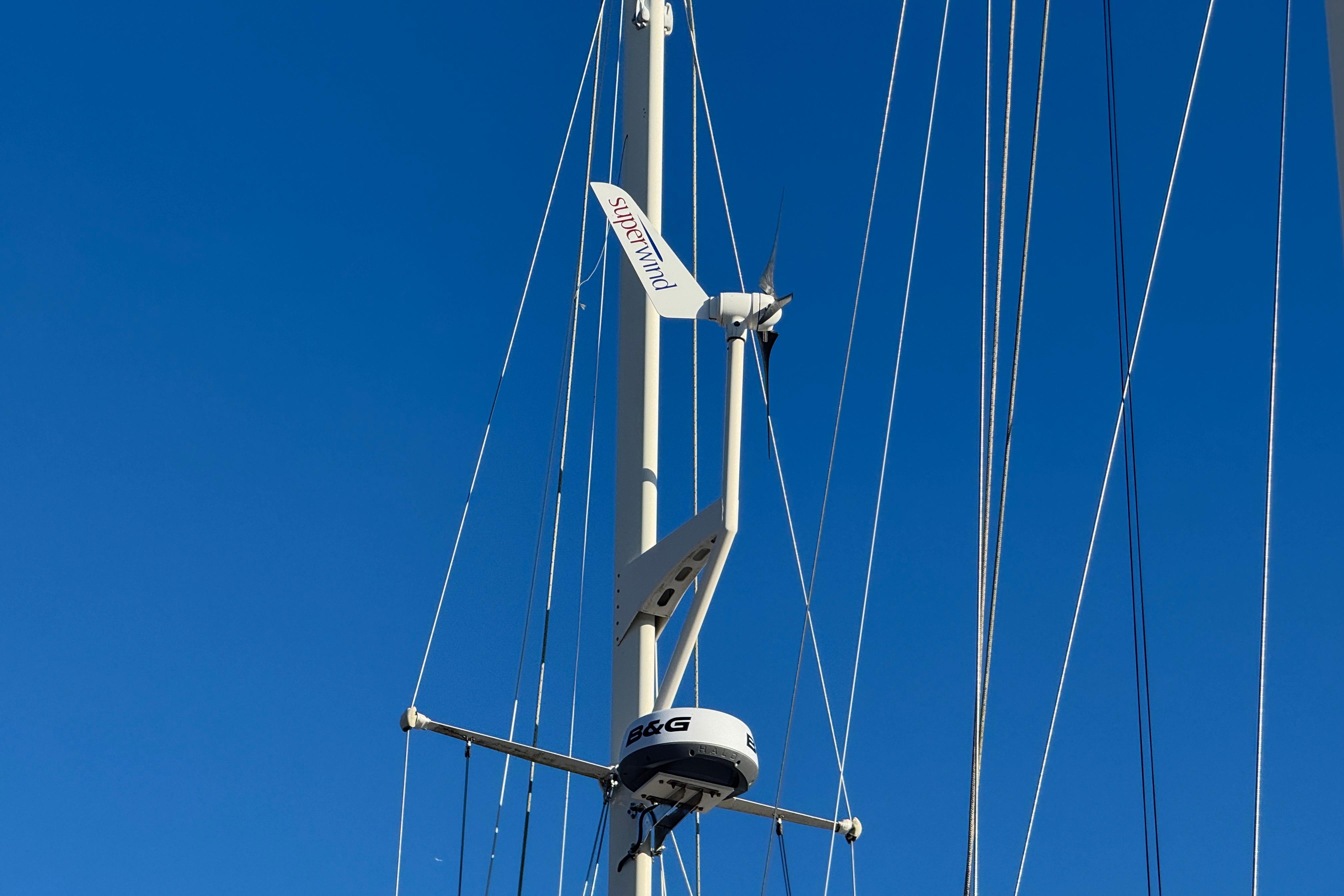 Mast of 1988 Amel Sharki sailboat with Superwind turbine against clear blue sky.