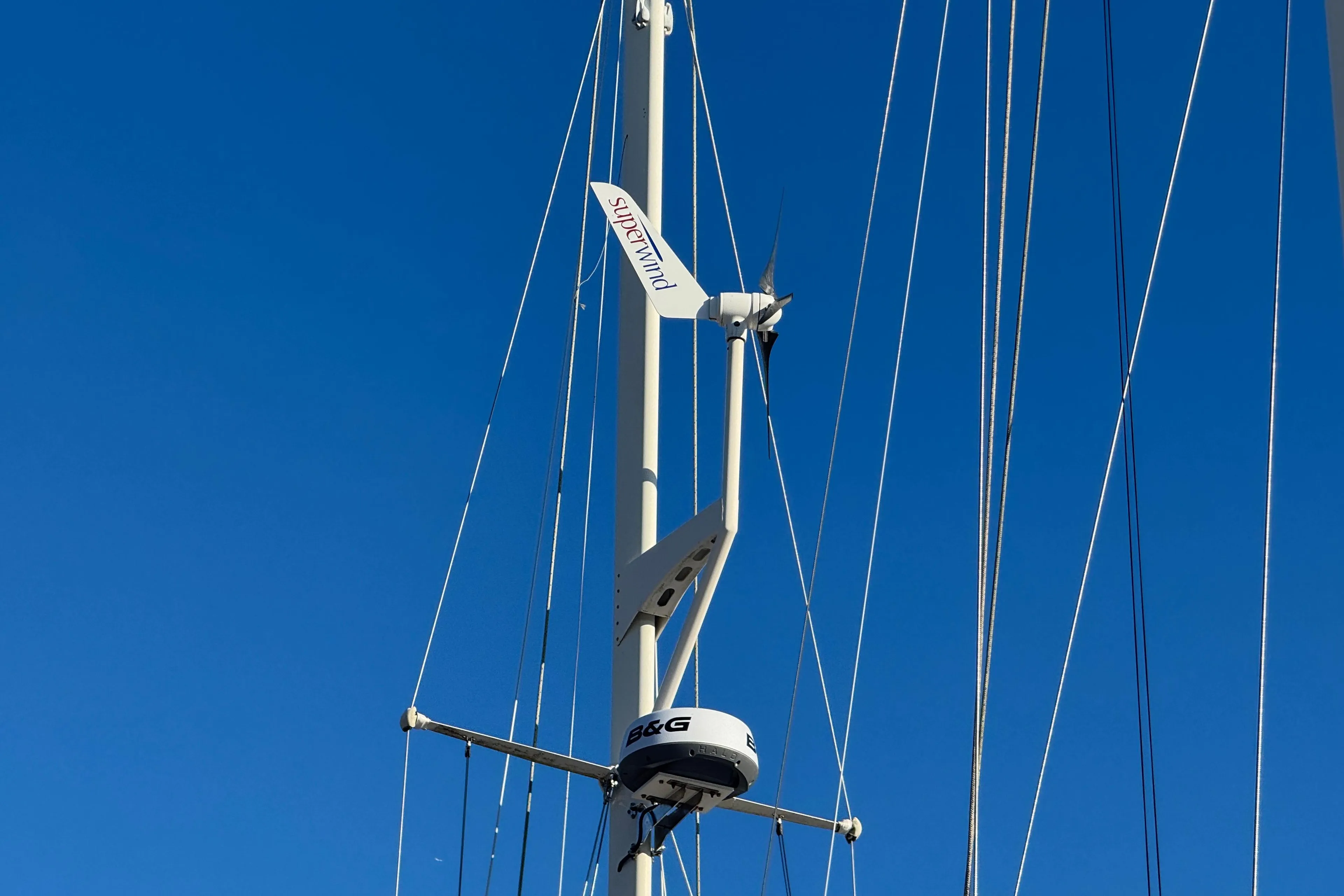 Mast of 1988 Amel Sharki sailboat with Superwind turbine against clear blue sky.