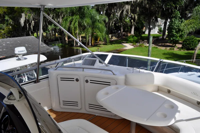 King Leisure Yacht Photos Pics 2002 Sea Ray 480 Sedan Bridge yacht interior with seating and table, surrounded by lush greenery.