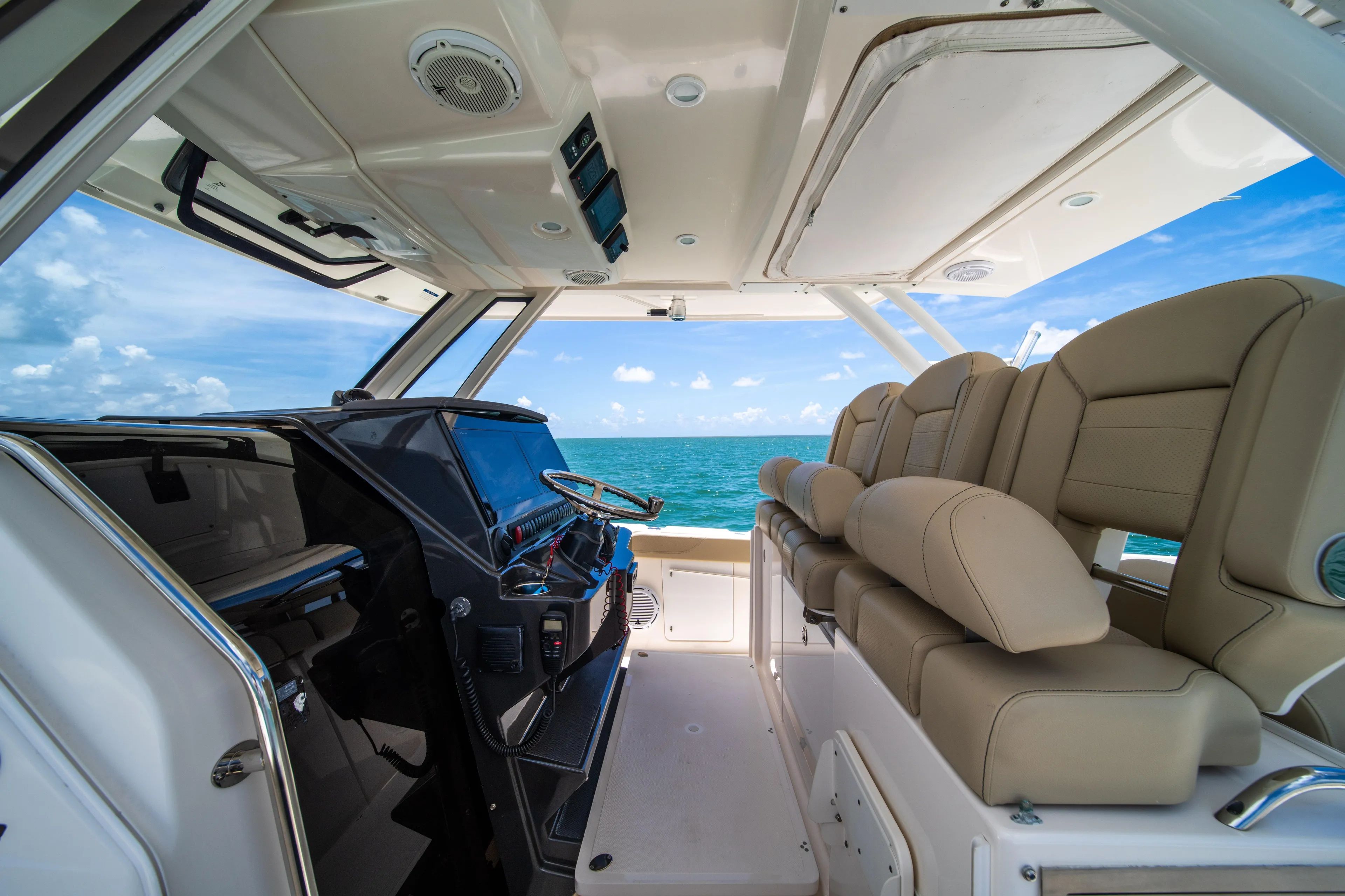 100 Percent Yacht Photos Pics 2018 Pursuit S 368 Sport boat interior with ocean view, featuring beige seating and modern controls.