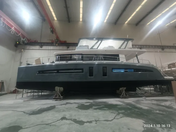  Yacht Photos Pics 2024 Mazarin 55 Catamaran Hybrid in a shipyard, under bright industrial lighting.