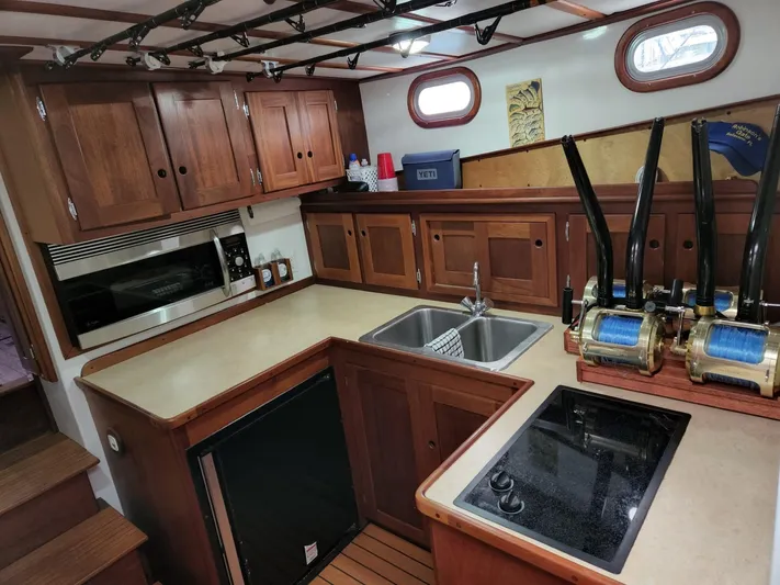 Ahi Ink Yacht Photos Pics 2003 Wesmac Flybridge kitchen with wooden cabinets, dual sink, and fishing reels.
