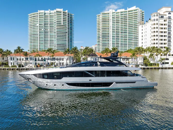 Beso Yacht Photos Pics 2024 Riva 102 Corsaro Super yacht cruising near luxury waterfront buildings.