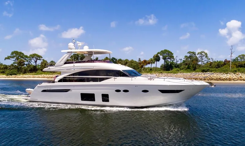 Clarity Yacht Photos Pics 2015 Princess Flybridge 68 Motor Yacht cruising on a sunny day near a lush shoreline.
