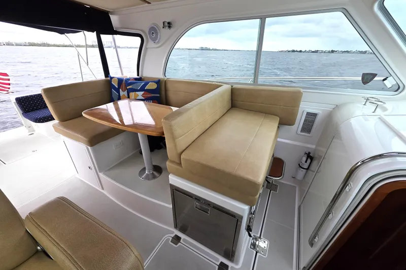 Jubilee Yacht Photos Pics 2018 Back Cove 32 yacht interior with beige seating and wooden table, overlooking the water.