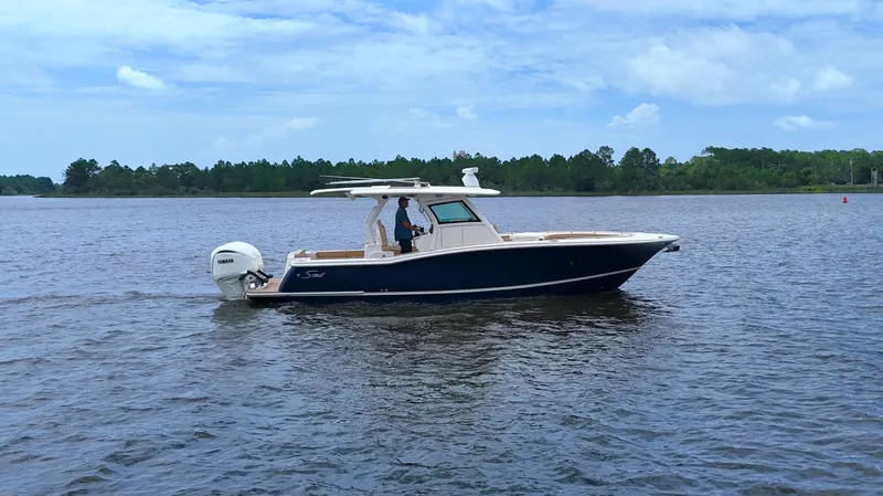 Engine Warranty X Trailer Yacht Photos Pics 2022 Scout 330 LXF boat cruising on a calm lake under a clear blue sky.