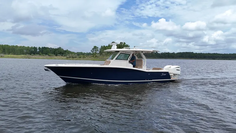 Engine Warranty X Trailer Yacht Photos Pics 2022 Scout 330 LXF boat cruising on a calm lake under a cloudy sky.