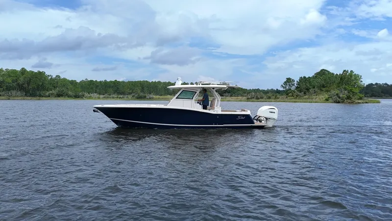 Engine Warranty X Trailer Yacht Photos Pics 2022 Scout 330 LXF boat cruising on a calm lake with lush green shoreline.