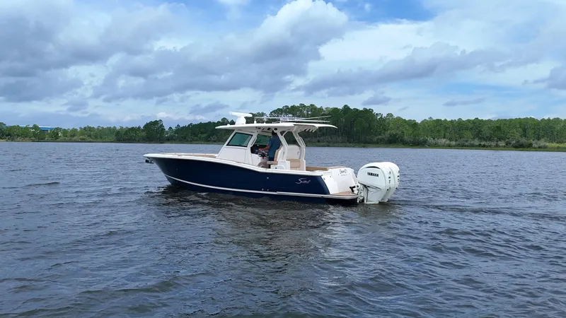 Engine Warranty X Trailer Yacht Photos Pics 2022 Scout 330 LXF boat cruising on a calm lake under a cloudy sky.