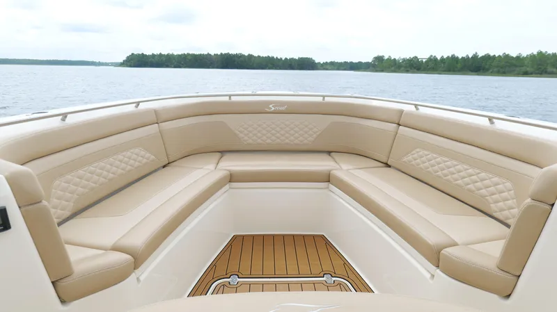 Engine Warranty X Trailer Yacht Photos Pics 2022 Scout 330 LXF boat interior with tan seating and wooden deck, on a calm lake.