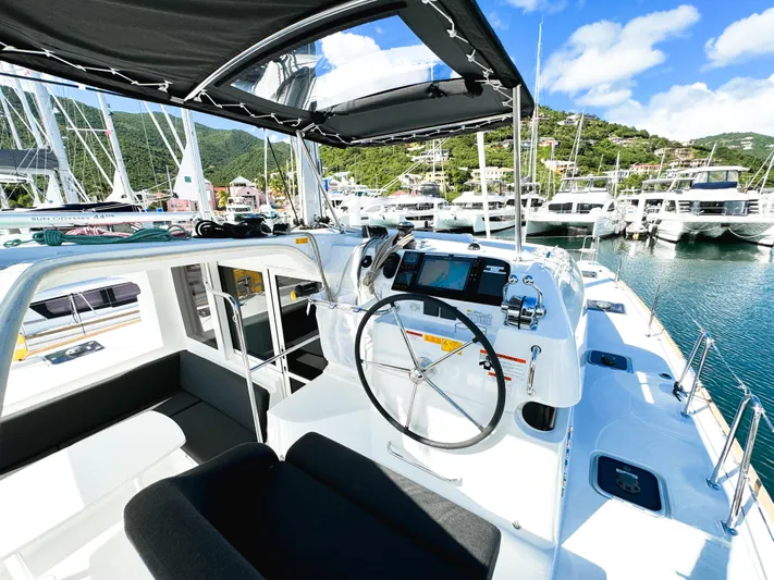 Cloud Walker Yacht Photos Pics 2024 Lagoon 40 catamaran cockpit with steering wheel, marina view, and blue sky.
