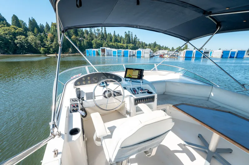  Yacht Photos Pics 1997 Bayliner 3988 yacht helm with navigation equipment, docked near blue boathouses and lush trees.