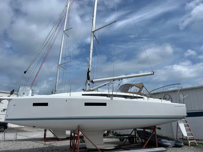  Yacht Photos Pics 2025 Jeanneau Sun Odyssey 380 sailboat on stands, under a cloudy sky.