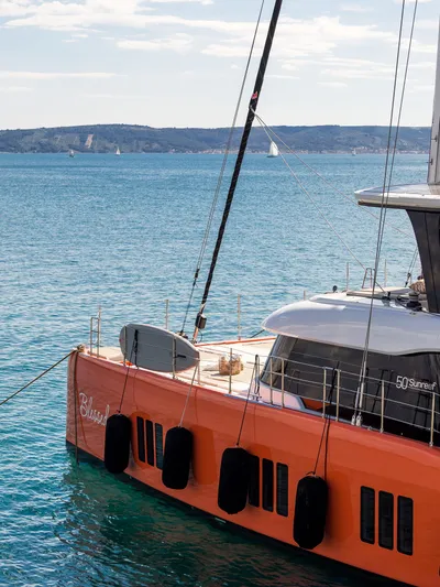 Blessed Yacht Photos Pics 2024 Sunreef 50 A yacht with vibrant orange hull, docked in serene blue waters.