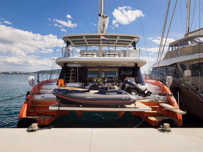 Blessed Yacht Photos Pics 2024 Sunreef 50 A yacht docked with tender boat, under clear blue sky.