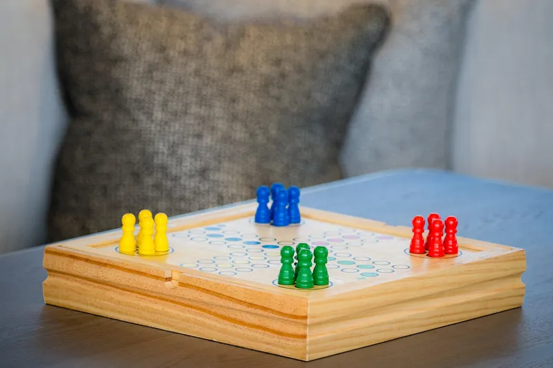 Blessed Yacht Photos Pics Wooden board game with colorful pieces on a table, featuring yellow, blue, green, and red pawns.