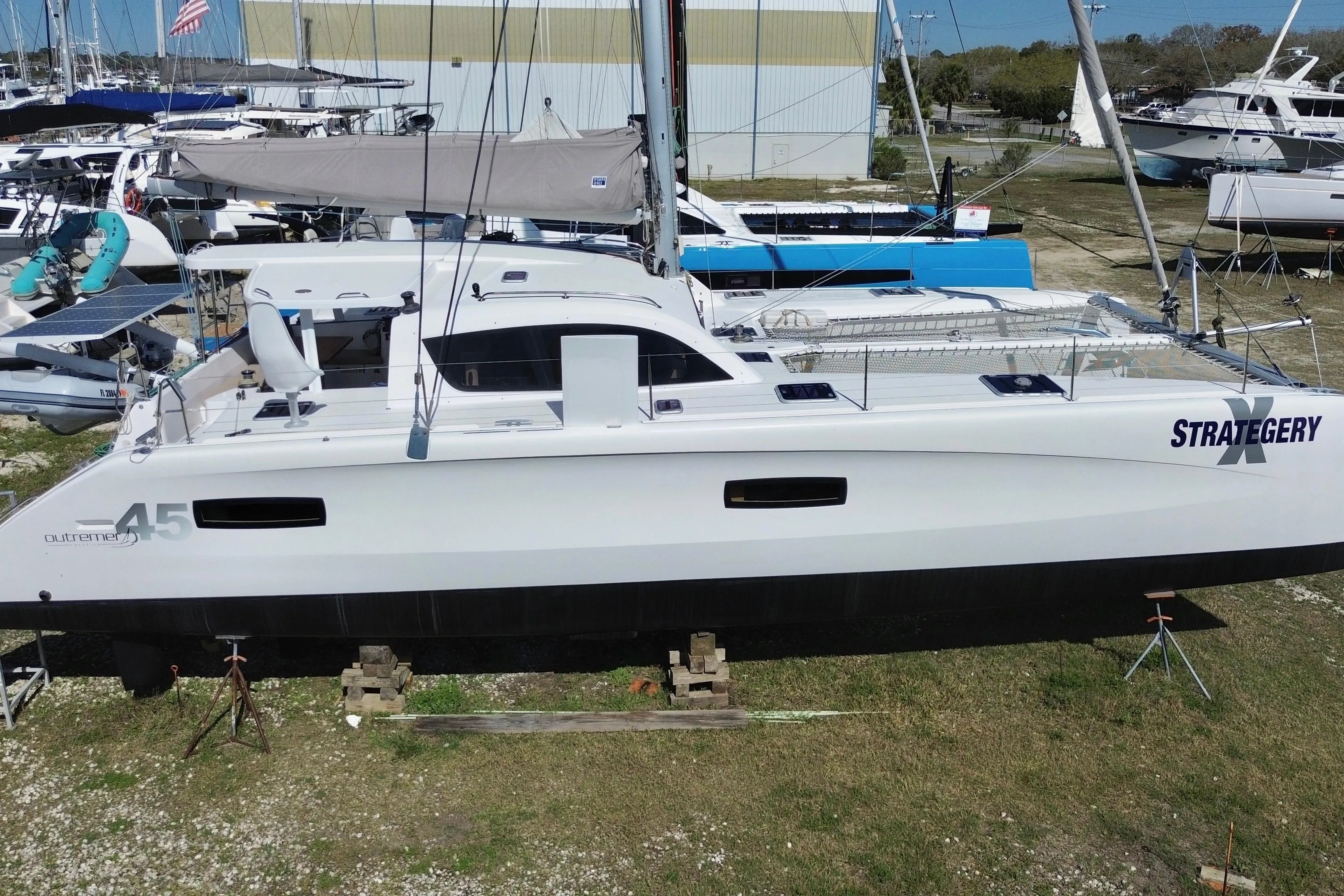 2014 Outremer 45 catamaran on land, white hull, named "Strategery," in a boatyard setting.