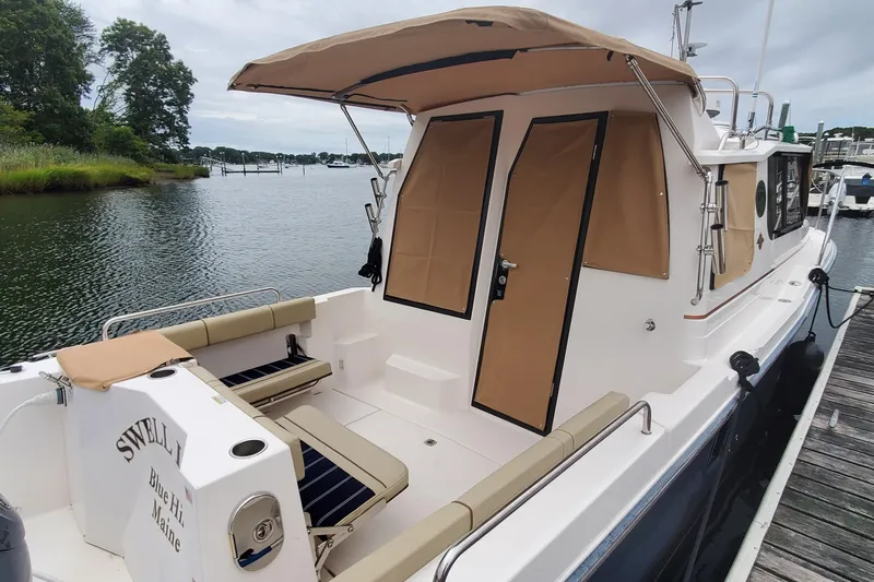 Swell Life Yacht Photos Pics 2021 Ranger Tugs R-25 boat docked, featuring tan canopy and seating, scenic waterfront view.