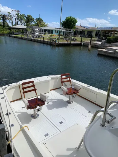 Legacy Yacht Photos Pics 1973 Bertram 31 Flybridge Cruiser with wooden chairs, docked by a serene waterfront.