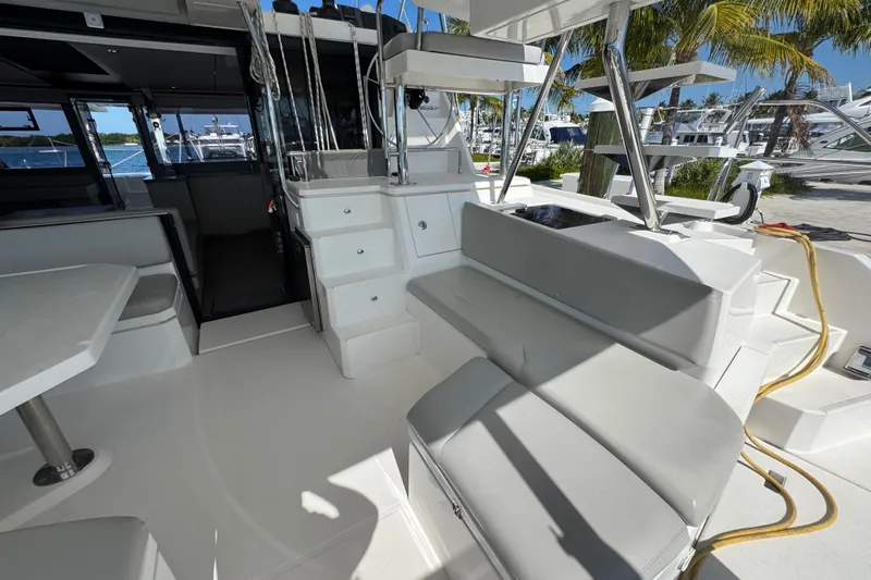 Ce Ya Yacht Photos Pics Spacious deck of 2021 Leopard 45 catamaran with seating and table, docked near palm trees.