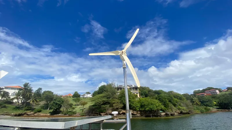 Certitude Yacht Photos Pics Wind turbine on a 1998 Fountaine Pajot Bahia 46 catamaran, with lush coastal scenery.