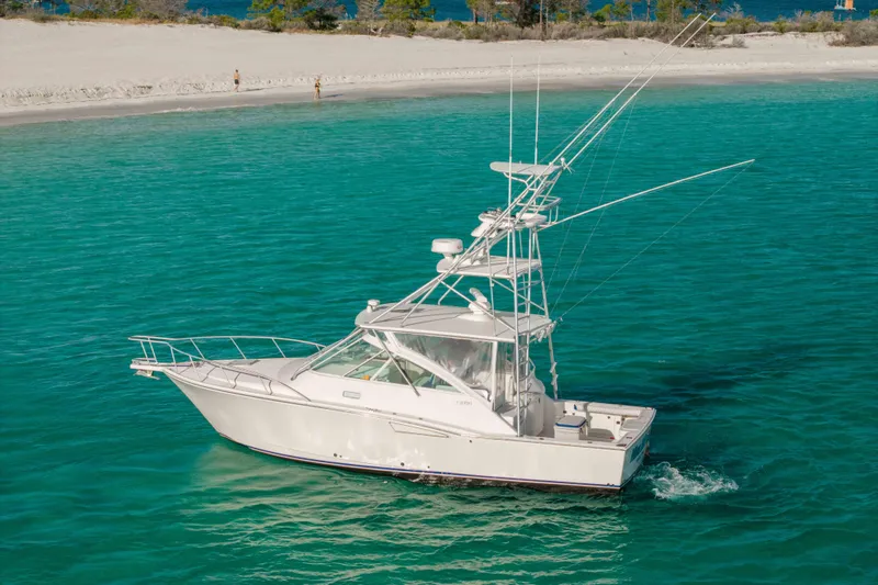Miss Big Gun Yacht Photos Pics 2000 Cabo 35 Express boat cruising in clear turquoise waters near a sandy beach.