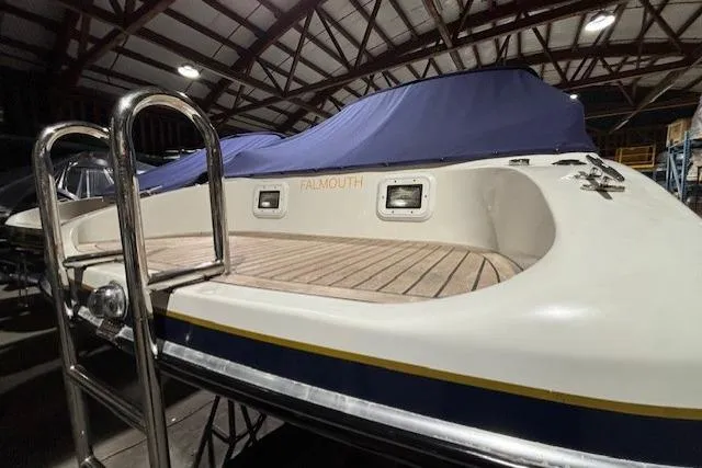 1998 Craig Craft Launch boat in a warehouse, featuring a wooden deck and covered seating area.